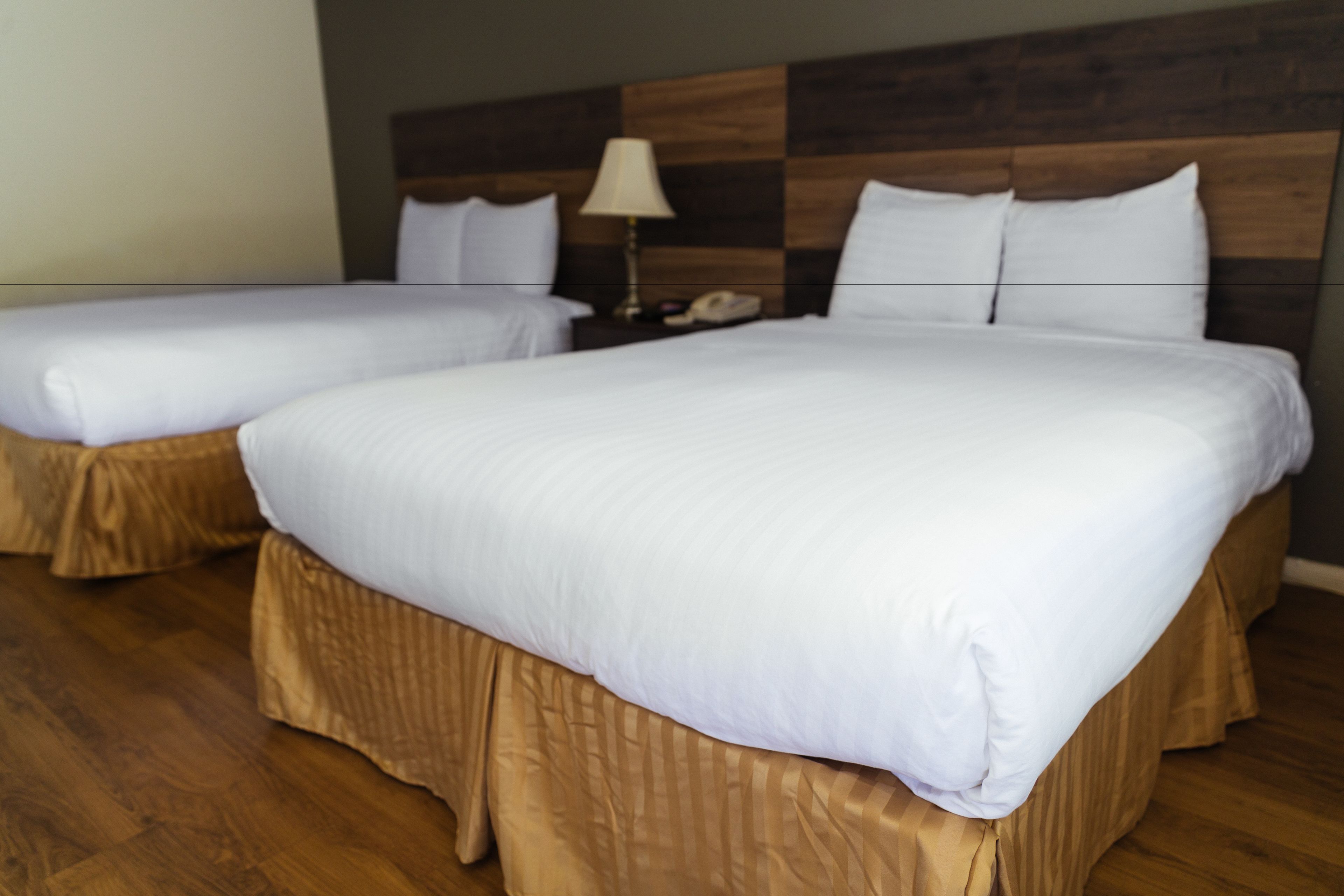 A hotel room with two beds, wooden headboard, white bedding, and a nightstand with a lamp.