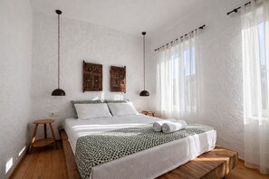 Ein Schlafzimmer mit einem Bett, zwei Wandlampen, einem Nachttisch und einem Fenster mit durchsichtigen Vorhängen.