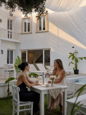Un patio al aire libre con mesa y sillas, piscina y un edificio blanco con ventanas y balcones.