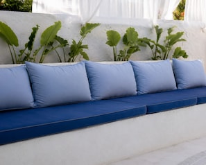 A blue cushioned bench with a white wall and green plants in the background. - Kozanogluhan Boutique Hotel (Cesme)