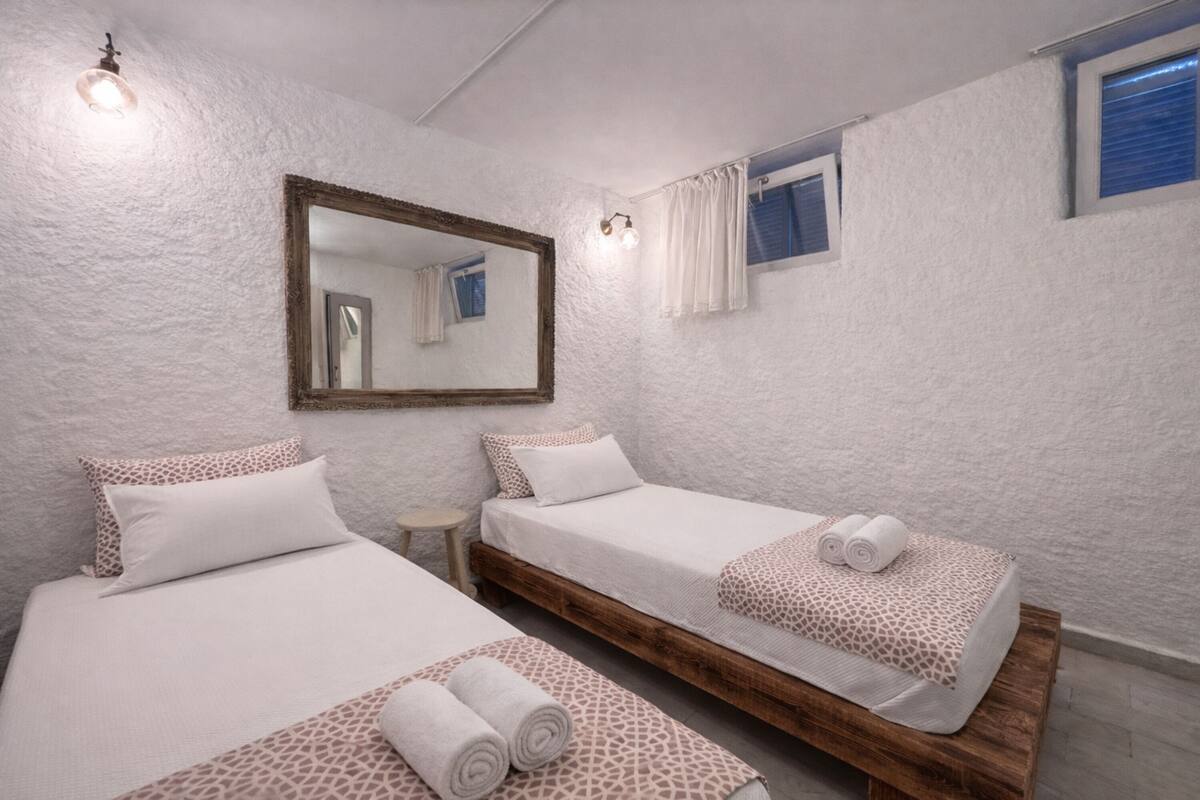 A room with two beds, a large mirror, a small table, and a window with curtains.