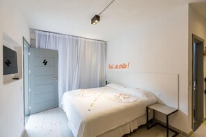 A bedroom with a bed, bedside table, and a door with a number. - Pousada Vila Quarta Praia (Cairu)