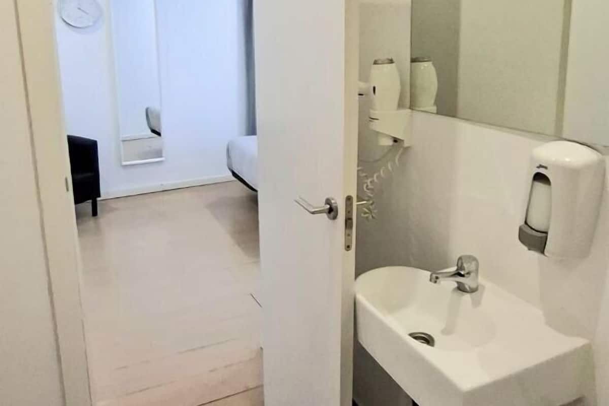 Un baño con un lavamanos blanco, un espejo y una puerta que da a un dormitorio.
