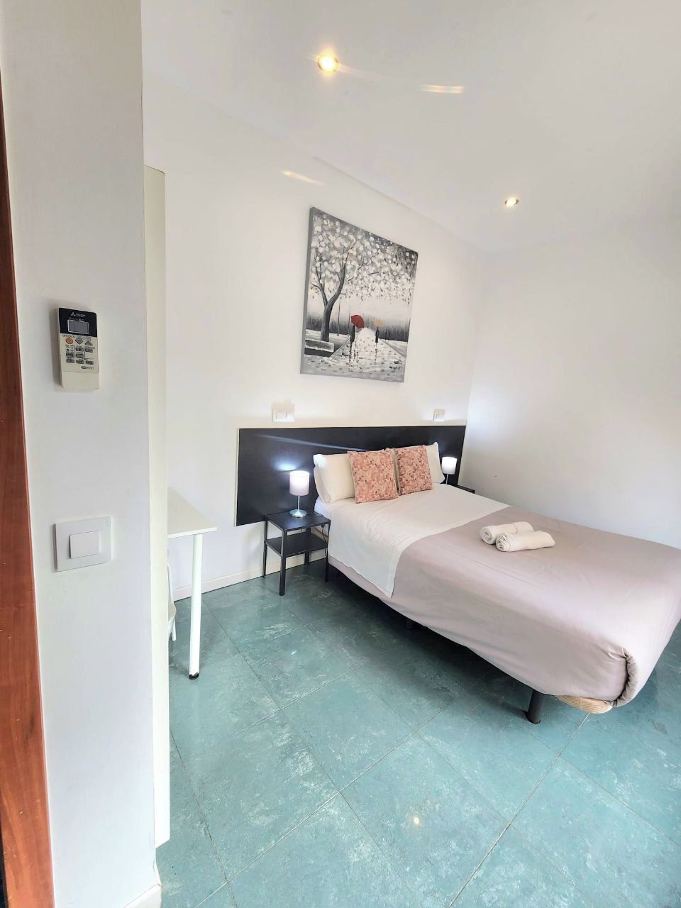 A hotel room with a bed, a desk, a chair, a nightstand, and a painting on the wall.