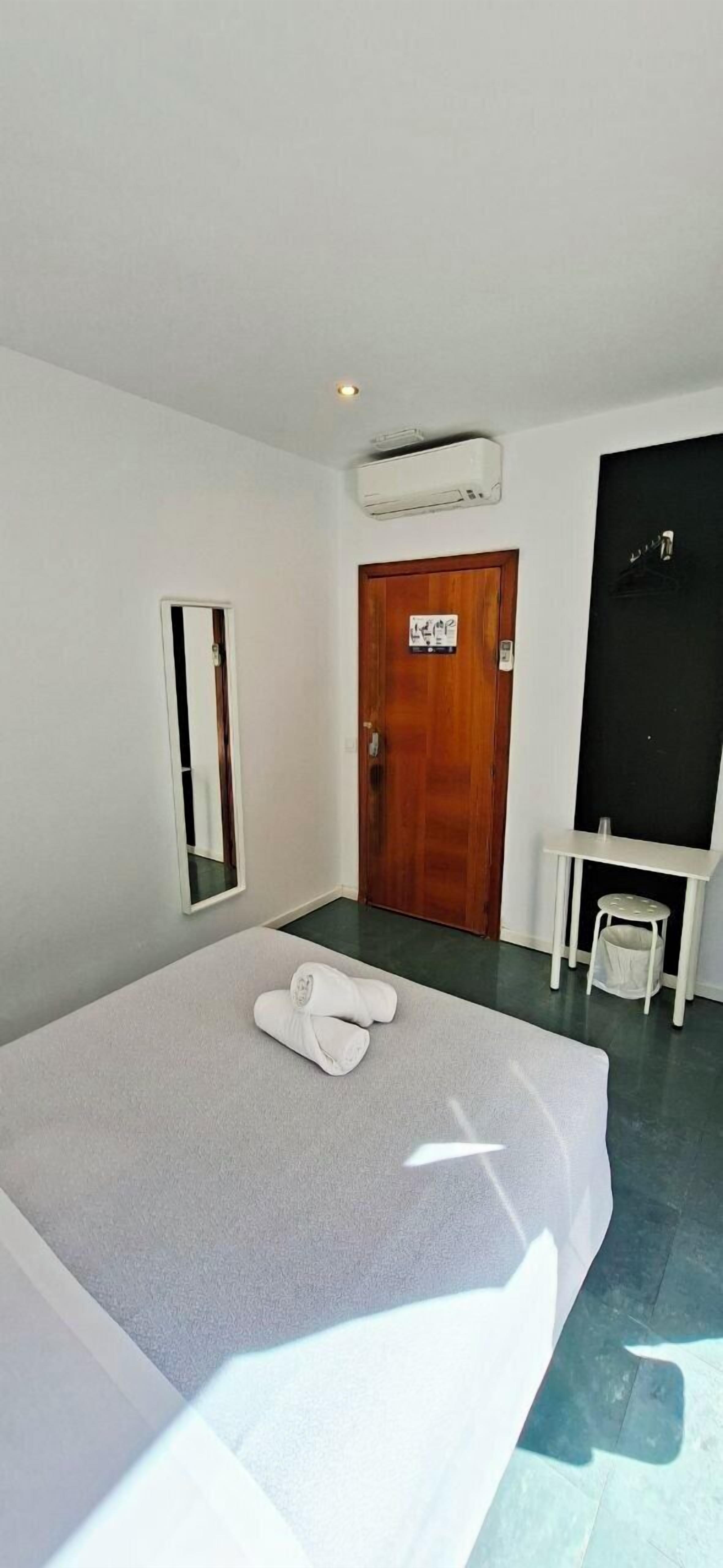 A hotel room with a bed, a wooden door, a small table, and a mirror.