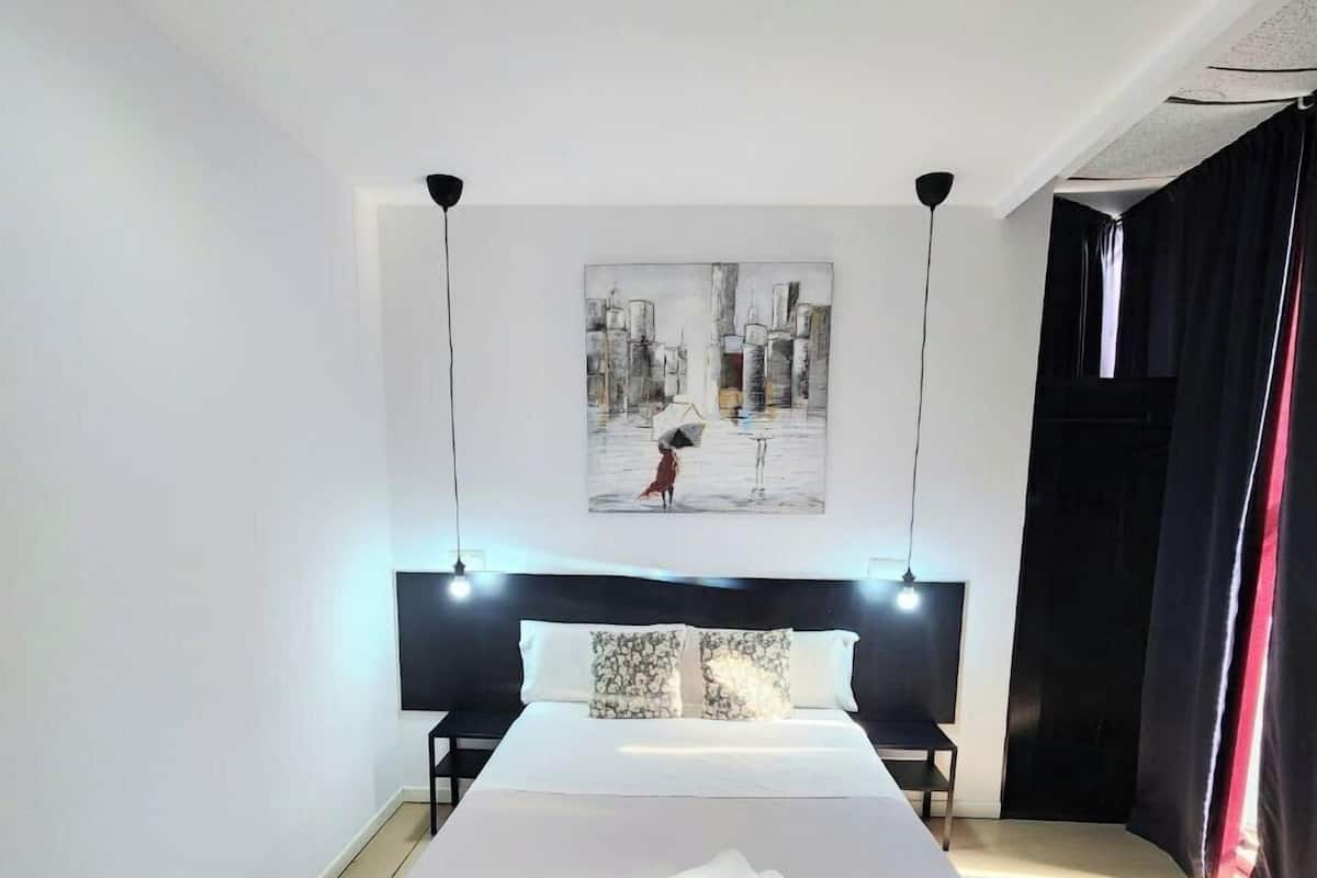 Habitación de hotel moderna con una cama grande, un cuadro de paisaje urbano en la pared y una lámpara de pie negra.
