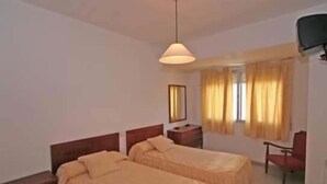A hotel room with two single beds, a bedside table, a chair, a TV, and a window with curtains. - Hotel Angelito (O Grove)