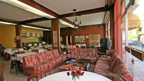 A dining area with a large table, red patterned sofas, and a TV. - Hotel Angelito (O Grove)
