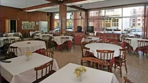 A dining area with round tables and chairs, large windows, and a view of the street outside. - Hotel Angelito (O Grove)