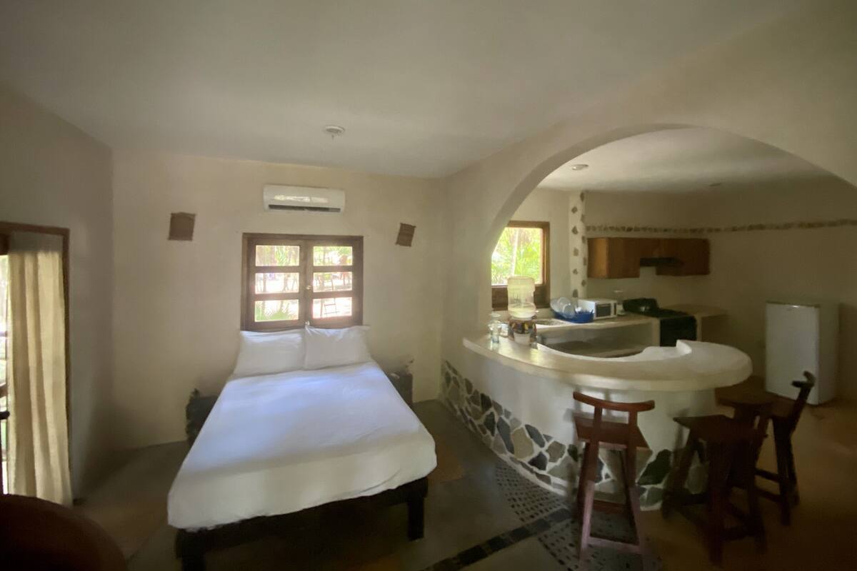Un dormitorio con una cama grande, un baño con lavamanos y espejo, y una zona de cocina.