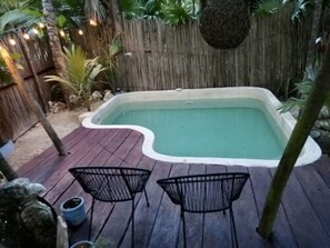A rectangular hot tub with a wooden deck surrounding it, two metal chairs, and a bamboo fence in the background. - MAYA Apartments Tulum (Tulum)