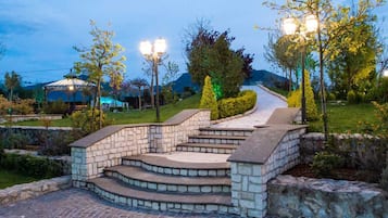 A stone staircase leading up a hill, surrounded by greenery and a gazebo in the background.