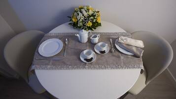 A round dining table with a white tablecloth, a vase of flowers, and a set of white plates, cups, and cutlery.