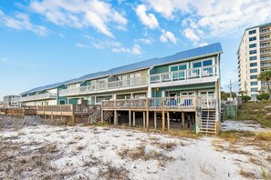 Een hotel aan het strand met meerdere balkons, een houten terras en een zandstrand.