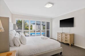 A bedroom with a large bed, a dresser, a flat-screen TV, and a window with blinds. - Cowes - Modern 5 Bedroom house with solar heated swimming pool, spa & sauna  (Cowes)
