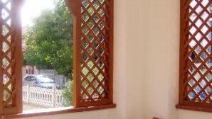Una habitación con ventanal de celosía, una mesa con mantel tejido y varias plantas en macetas.