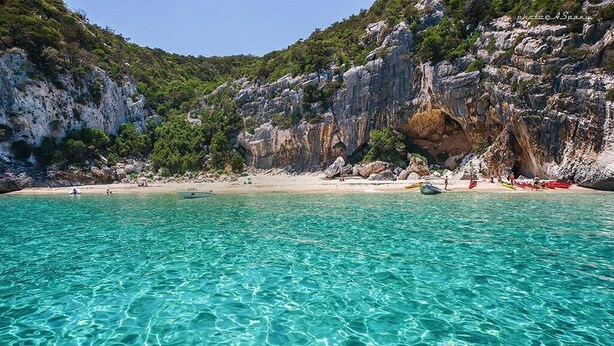 Una playa costera con agua turquesa cristalina, acantilados rocosos y una orilla arenosa.