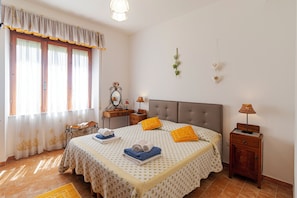 A bedroom with a bed, bedside tables, a nightstand, a lamp, a mirror, and a window with curtains.