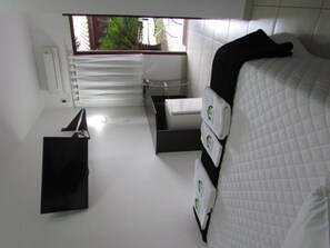 A small, modern bathroom with white tiles, a window with a view of greenery, a radiator, and a black towel rack. - Pousada Remanso (Bonito)