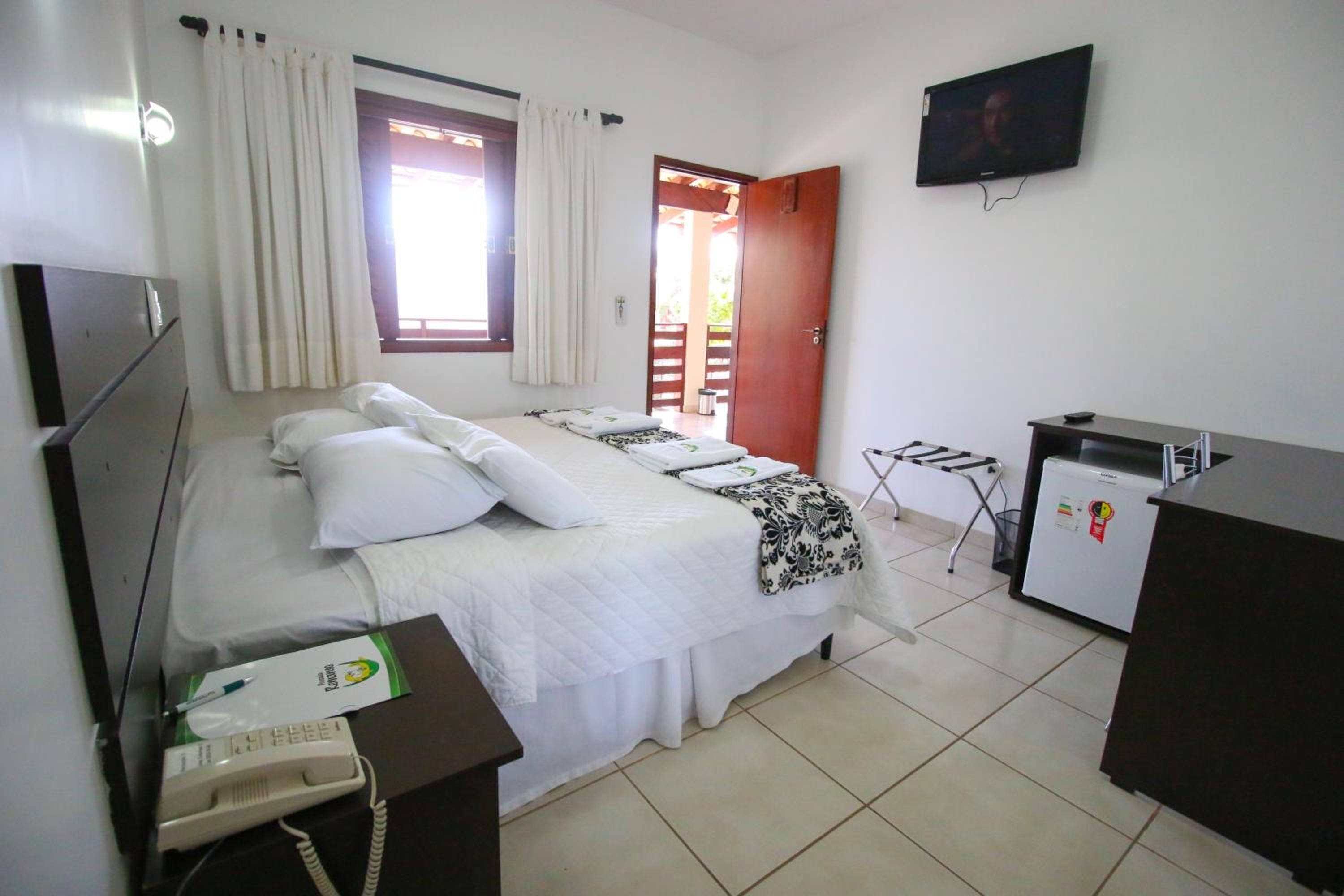 Una habitación de hotel con una cama, un escritorio con teléfono, televisor y refrigerador.
