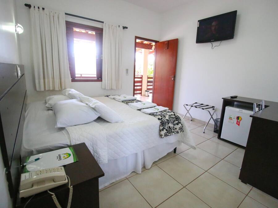 Una habitación de hotel con una cama, un escritorio con teléfono, televisor y refrigerador.