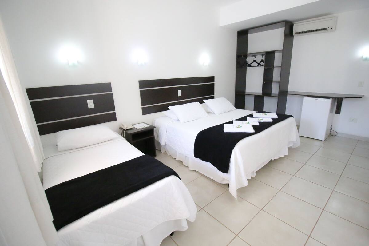 A hotel room with two beds, a desk, and an air conditioning unit.