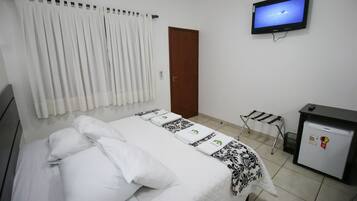A hotel room with a bed, a television on the wall, a desk with a refrigerator, and a window with curtains.