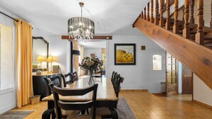 Un comedor con una mesa de madera, sillas, una araña y una escalera.