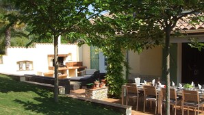 Un patio al aire libre con una mesa de comedor preparada para cuatro personas, rodeado de muebles de mimbre y plantas en macetas.