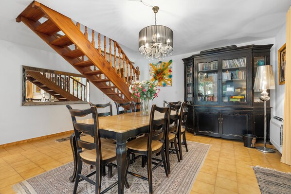 A dining room with a wooden staircase, a chandelier, and a bookcase.