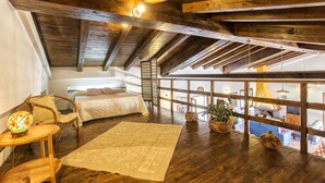 A cozy loft bedroom with exposed wooden beams, a large window, a bed, a chair, and a table with a lamp. - Splendid independent Villa surrounded by Sardinian nature (Putifigari)