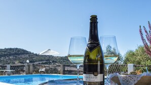 A bottle of Torbato wine, two glasses, and a basket of food on a table by a pool with a view of hills. - Splendid independent Villa surrounded by Sardinian nature (Putifigari)