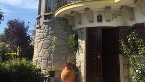 Ein zweistöckiges Gebäude mit einer Stein-Fassade, einem Balkon mit Sonnenschirm und einer großen Pflanze im Topf davor.