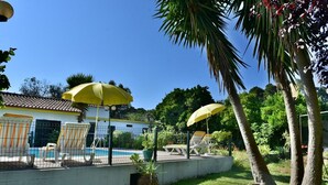 Ein Poolbereich mit gelben Sonnenschirmen, Liegestühlen und einem Gebäude mit blau-weiß gefliestem Dach.