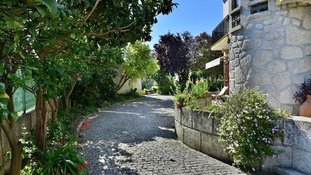 Ein Pflasterweg, gesäumt von üppiger Vegetation und einem Steinhaus mit Balkon.