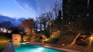 Una piscina con pared de piedra y cubierta de madera, rodeada de árboles y otra pared de piedra.