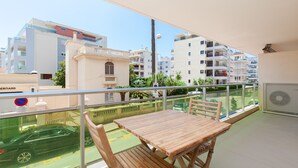 A balcony with a wooden table and chairs, overlooking a street with cars and buildings.