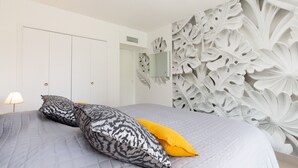 A bedroom with a bed, pillows, a nightstand, a lamp, and a decorative wall panel.