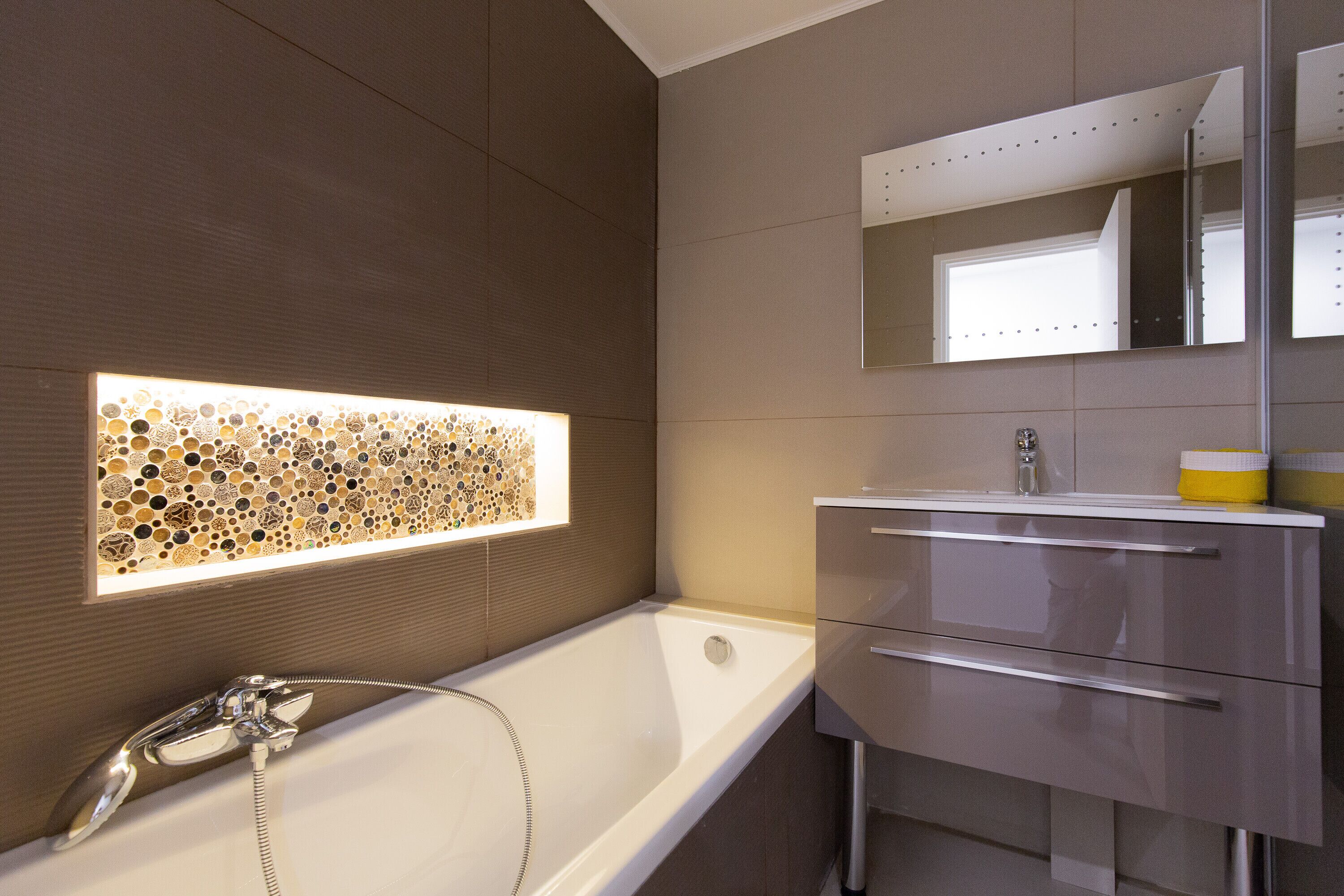 Une salle de bain moderne avec une baignoire, un miroir fixé au mur et un meuble-lavabo avec des tiroirs.