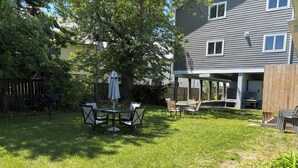 A backyard with a covered patio table and chairs, surrounded by a well-maintained lawn and trees.