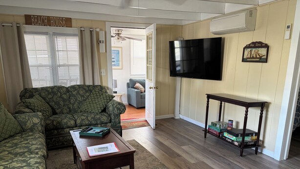 A living room with a sofa, a coffee table with remotes, a TV, and a small table with books and cans.
