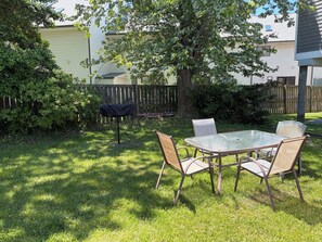 A backyard with a glass table and chairs, surrounded by grass and a wooden fence. - ￼Centrally Located Dewey Cottage - 1.5 Blocks to the Beach  (Dewey Beach)