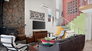 A living room with a stone wall, a flat-screen TV, a sofa, a chair, and a staircase. - Clear Creek Retreat - Take a trip to the mountains (Georgetown)