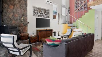 Un salon avec un mur en pierre, un téléviseur à écran plat, un canapé, un fauteuil et un escalier.