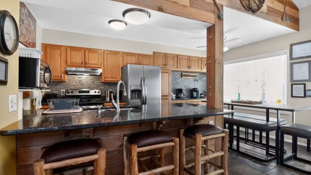 A kitchen with wooden cabinets, a stainless steel refrigerator, a large island with stools, and a hanging light fixture. - Clear Creek Retreat - Take a trip to the mountains (Georgetown)