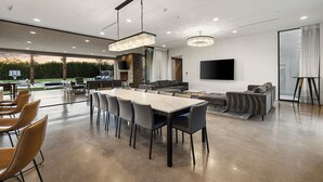 A modern living room with a large dining table, sofas, and a TV mounted on the wall. - Ultra Luxury Modern Villa w/ Pickleball, Basketball, Soccer, Heated pool & Spa (Paradise Valley)