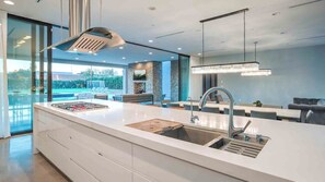 Enjoy cooking in this well-lit kitchen with a sleek island, range hood, and large windows overlooking a pool and outdoor seating area.