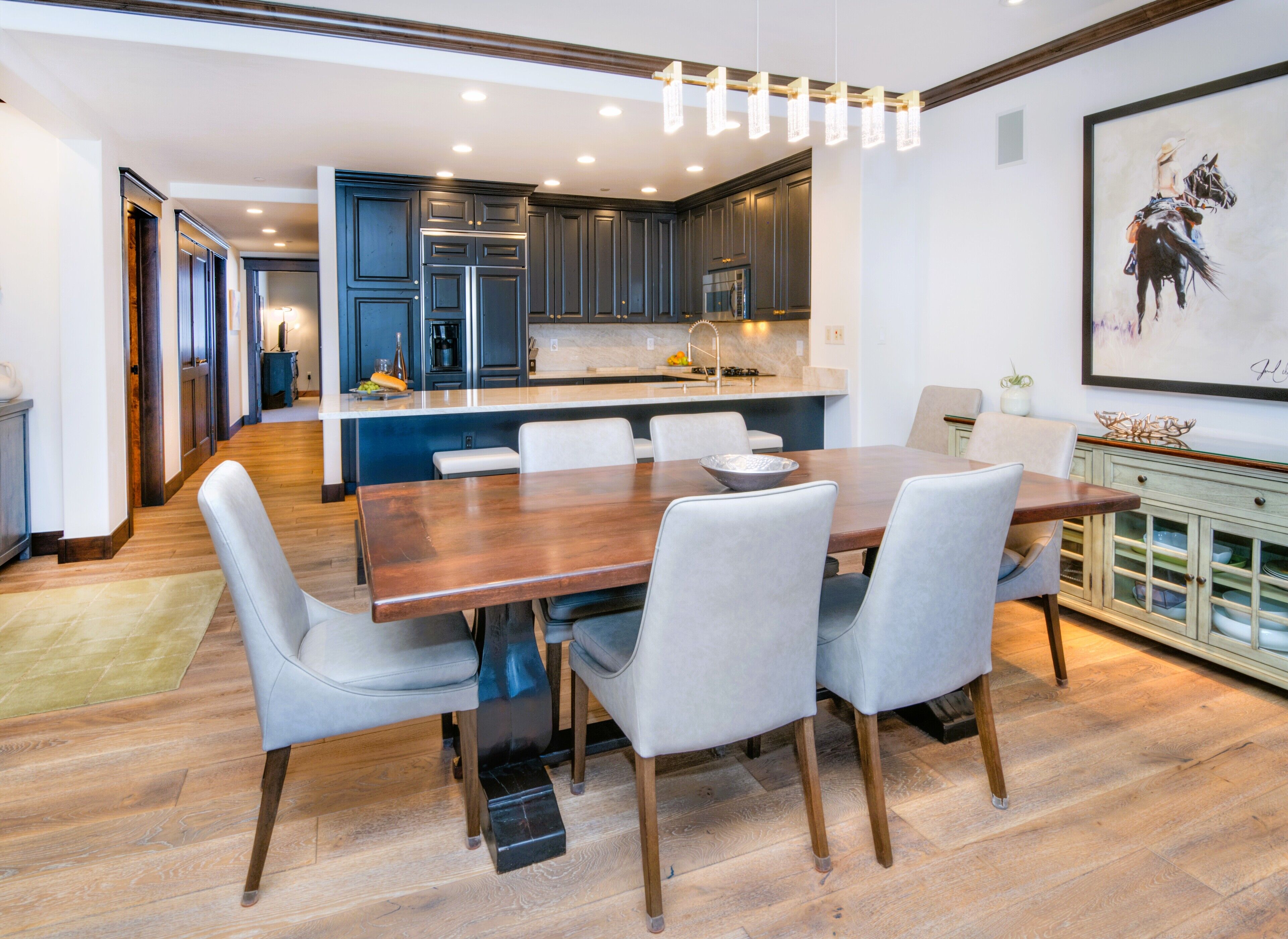 A modern kitchen with dark cabinets, a central island, and a dining area with a wooden table and chairs.