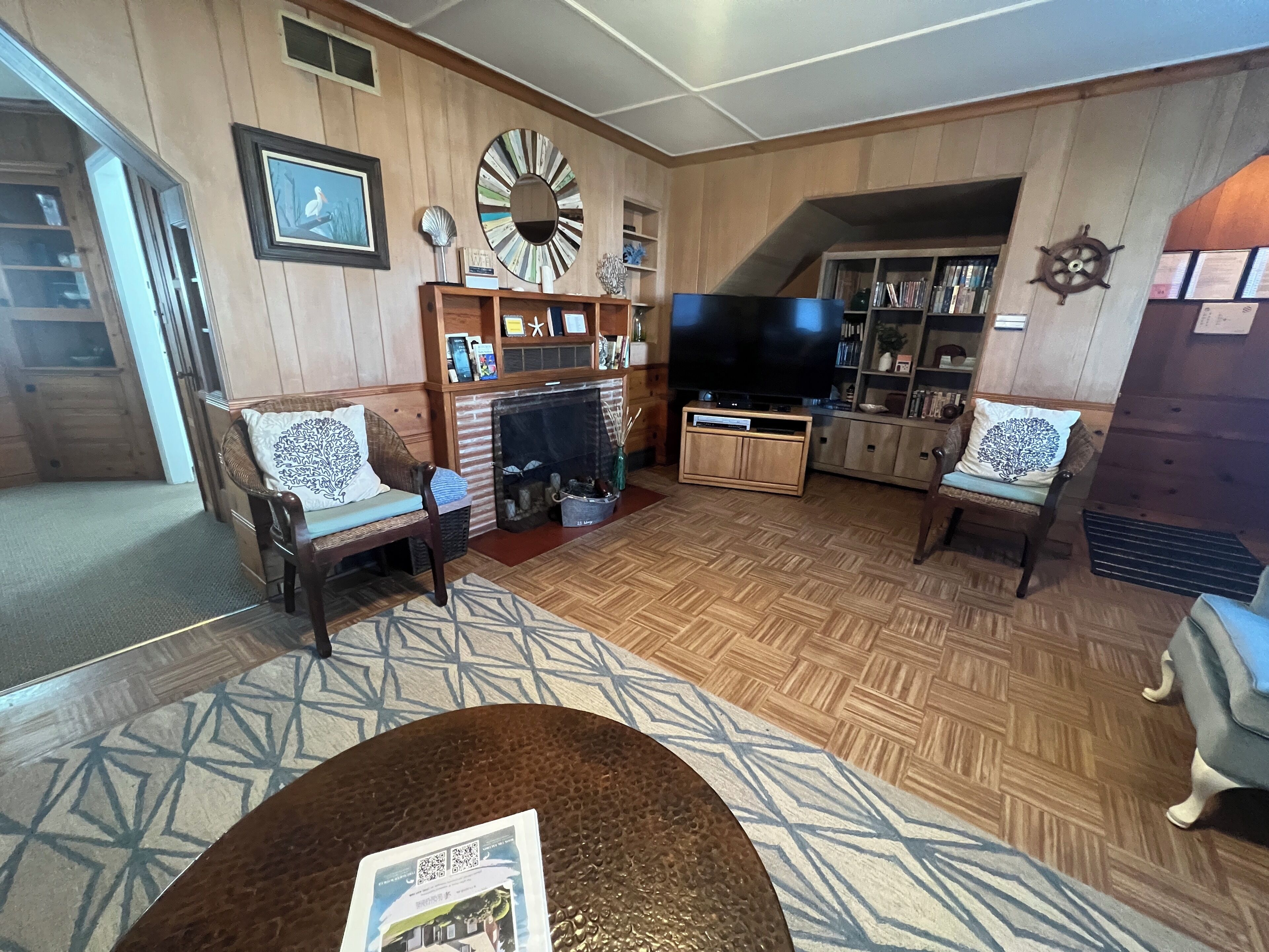 A living room with wooden walls, a fireplace, a television, and a bookshelf.