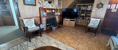 A living room with wooden walls, a fireplace, a television, and a bookshelf.